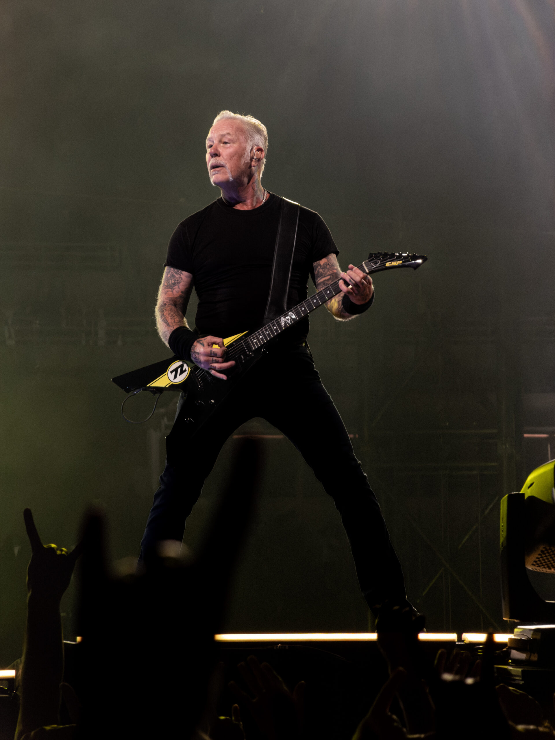 James Hetfield performing guitar during Metallica's M72 World Tour concert at OAKA Stadium, Athens, Greece, with fans raising devil horns in the foreground.