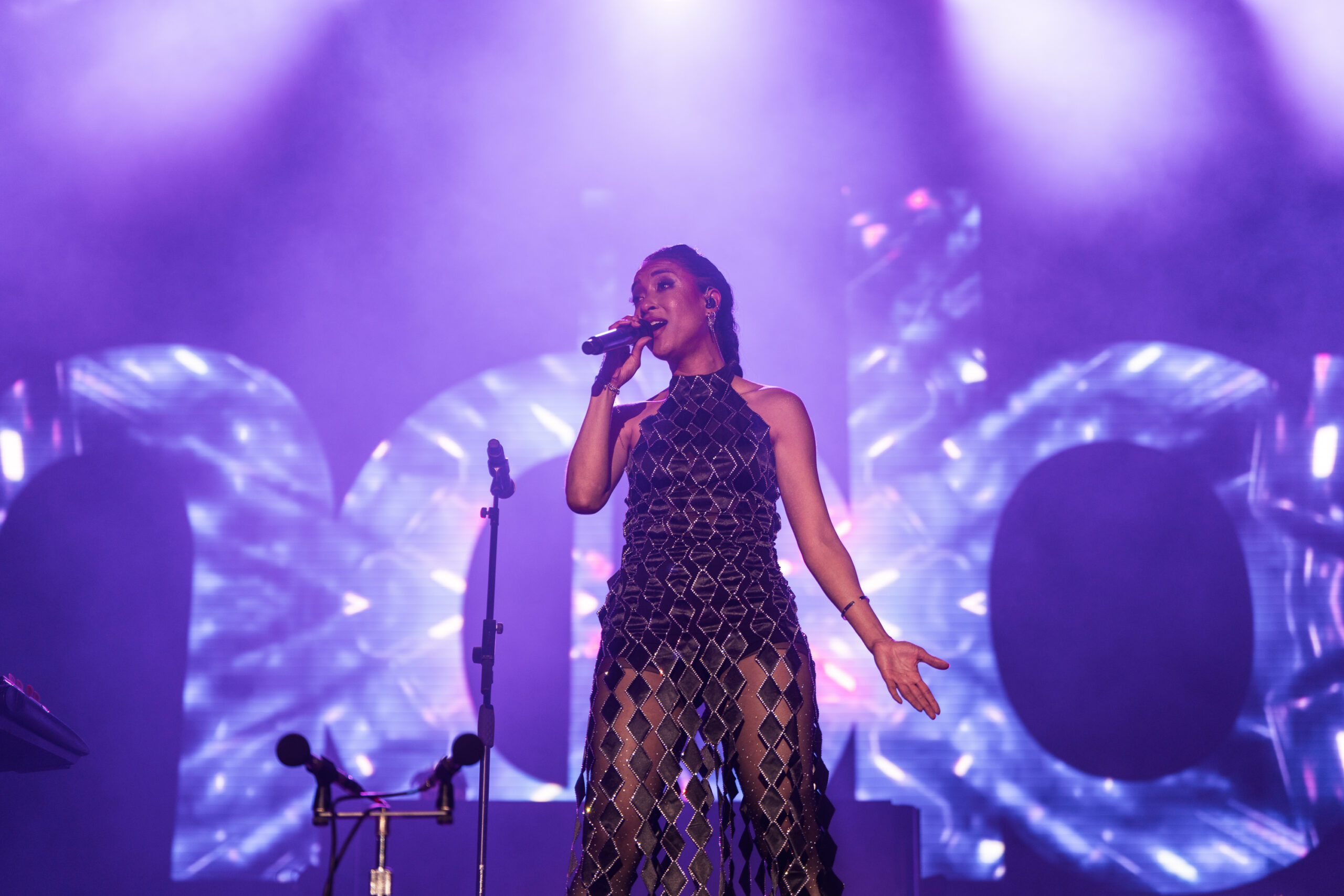 Nadia Christine Duggin singing into a microphone during Moby’s live show at Release Athens Festival 2026, with blue stage lighting and large visual projections in the background.