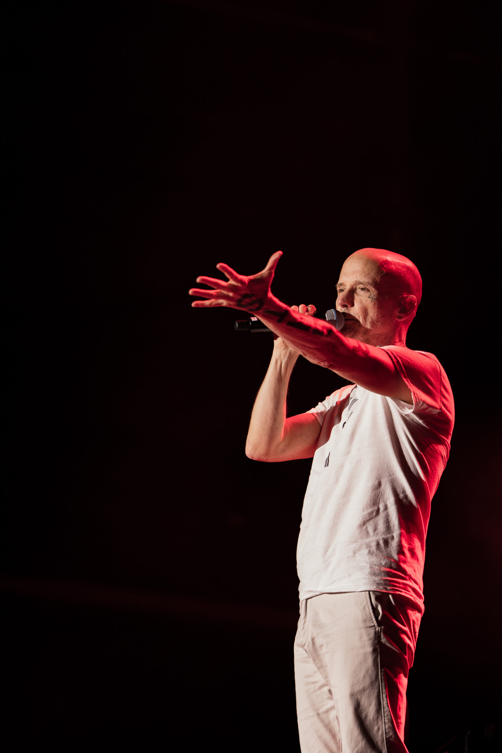 Moby speaking to the audience during his live show at Release Athens Festival 2026, reaching out with his hand under red stage lighting.