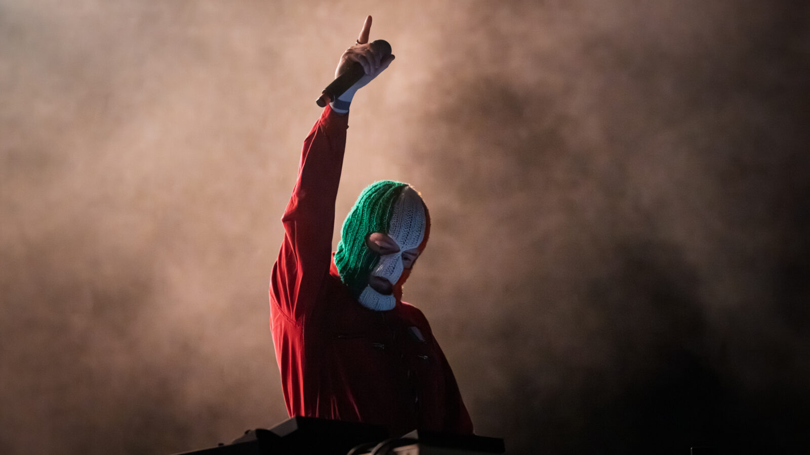 DJ Próvaí of Kneecap raising his arm on stage in an Irish tricolour balaclava during Rockwave Festival in Malakasa, Greece, 2026
